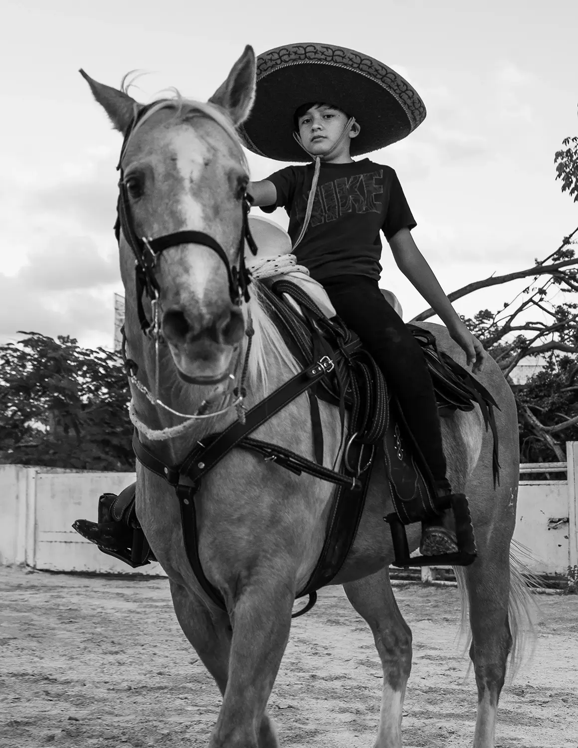 Black and White portrait of a boy with a typical mexican sombrero mounting a horse.