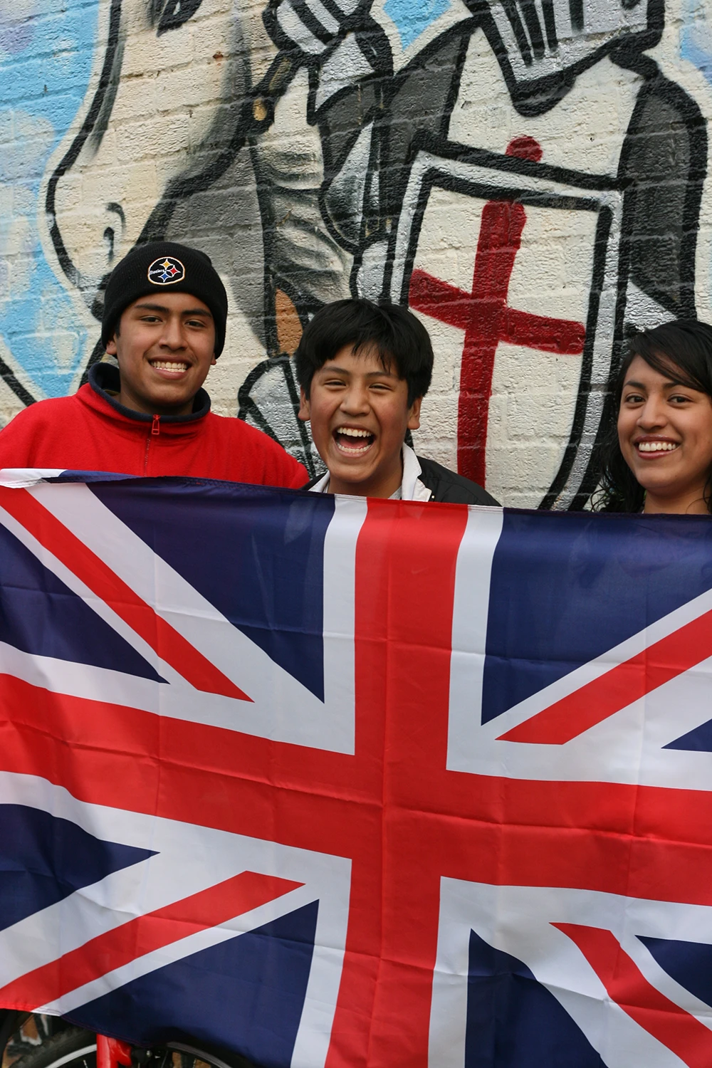 Teenagers posing in front of a graffiti mural of Saint George with the flag of the UK.