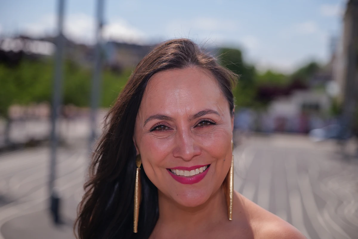Close-up portrait of a woman smiling at the camera while standing atop the hill at Den Sorte Plads in Copenhagen. The blurred background features the plaza’s iconic parallel white lines on asphalt.
