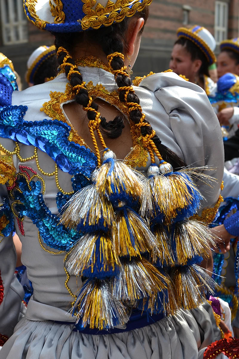 Back view of a woman dressed as a Caporalita, showcasing detailed hair braids adorned with vibrant blue, silver, and gold decorations.