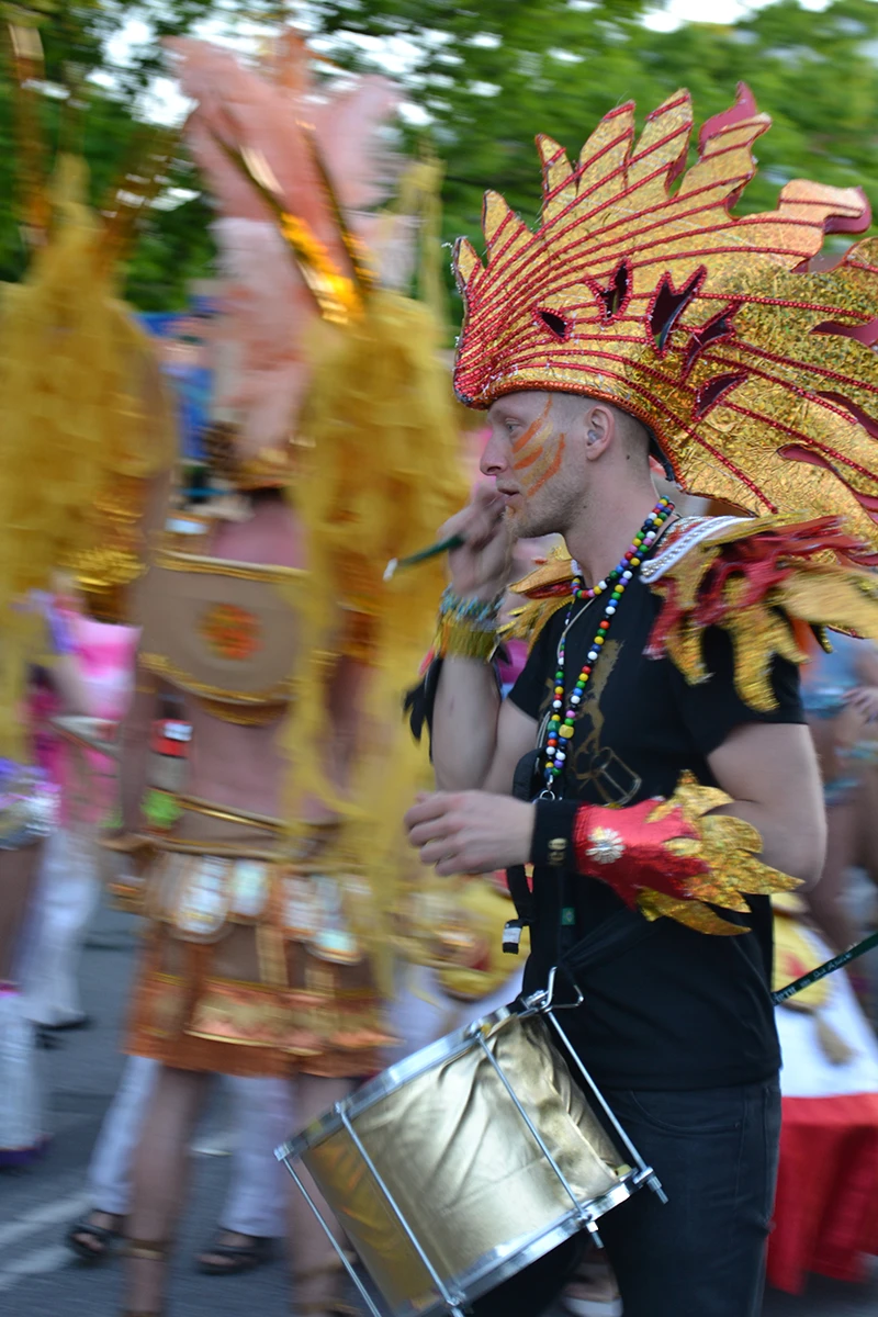 Young Scandinavian man in Rio Carnival costume carrying a drum at Copenhagen Carnival with Brazilian samba group.