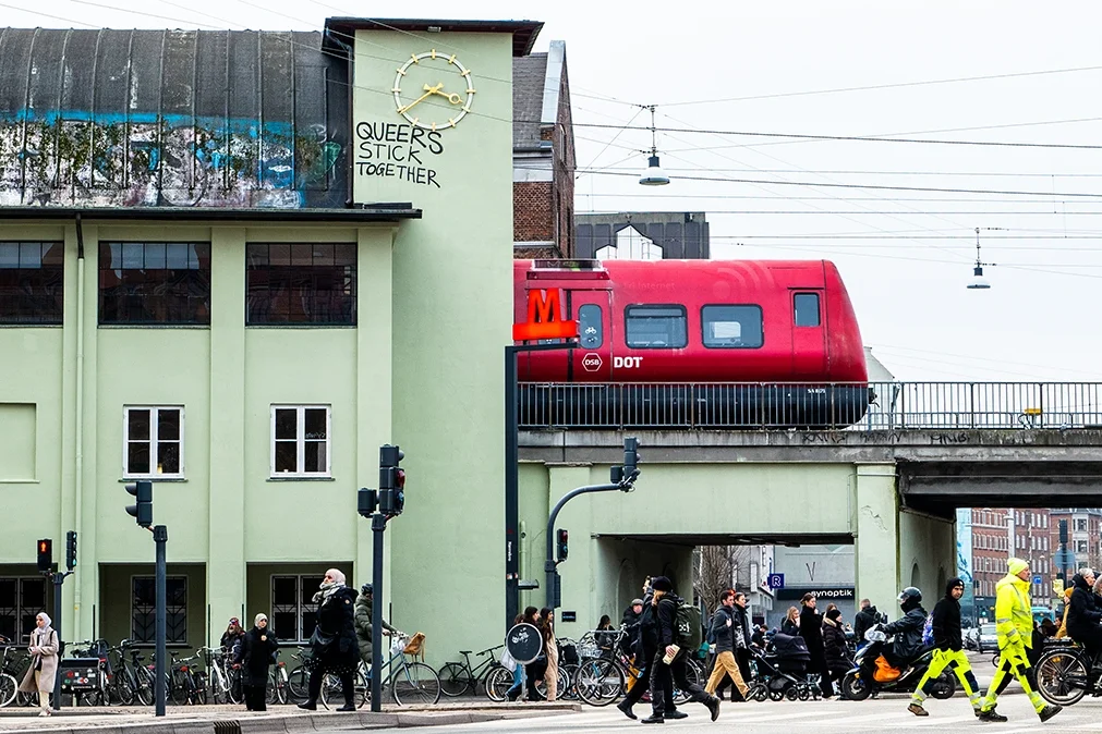 Red commuter train exiting Nørrebro Station in Copenhagen, Denmark, with platform and overhead wires visible.