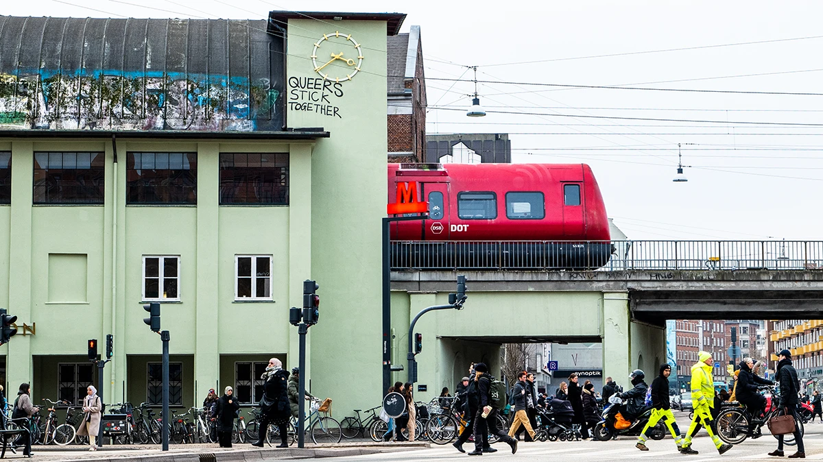 Red commuter train exiting Nørrebro Station in Copenhagen, Denmark, with platform and overhead wires visible.